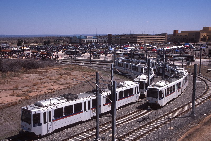 20130236-rtd.jpg - Two light rail trains simulataneously leaving the Federal Center Station.  The train in the "lead" is heading towards Golden, while the other train is on the turnback track.  During rush hours, every other train turns back at the Federal Center, providing 7.5-minute headways on the eastern section of the liner.  Federal Center is a major transfer point to buses, and the large parking lot in the background is full of cars and vendors for the opening festivities. (4/27/13)